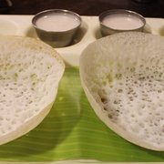 Two Appam pancakes served with coconut milk arranged neatly on a tray