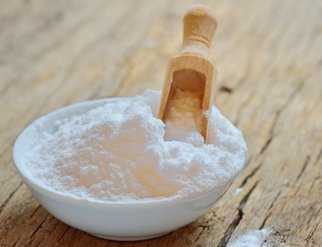 A bowl of baking soda with a wooden spoon resting on top, ready for use in baking or cooking