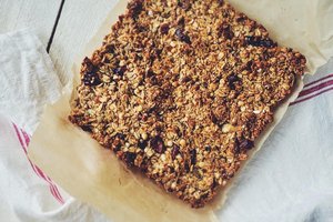 High-angle close-up view of a rectangular granola bar resting on a sheet of brown parchment paper, which is itself laid over a white linen cloth with thin red stripes