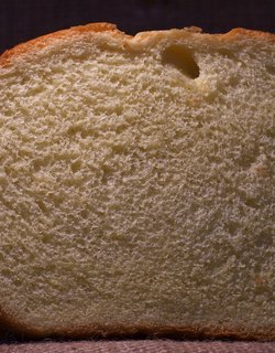 A slice of sandwich bread displayed on a brown background, highlighting its texture and color